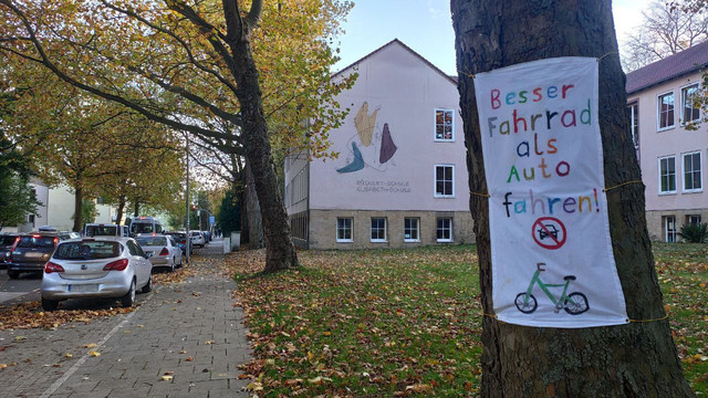 Elisabeth Schule in Osnabrück hängt selbst gestaltete Banner an Bäumen auf. 

Text Banner:
Besser Fahrrad als Auto fahren!
Links im Bild die Rückertstraße. Blickrichtung Kurt-Schumacher-Damm