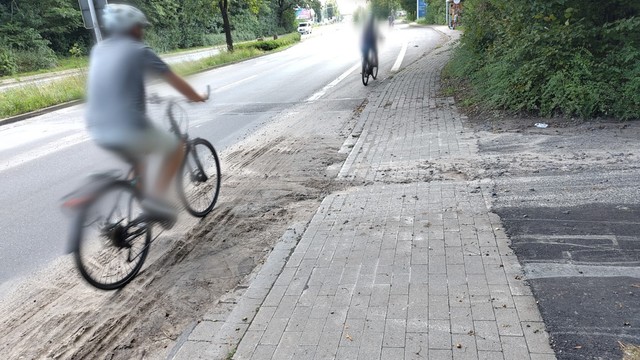 Kurt Schumacher Damm Fahrtrichtung stadtauswärts. Auf dem Radschutzstreifen liegt ein Erdesandgemisch. Ein Radfahrer fährt durch das Erdesandgemisch. In Richtung rechts geht es hoch zur Bredowstraße.