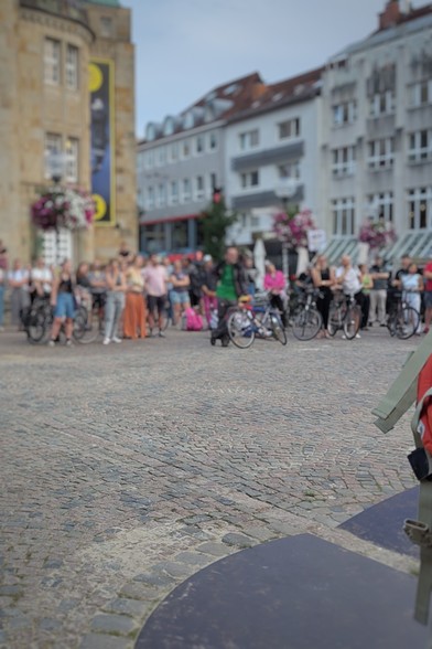 Zwischenkundgebung der Demo am Theater Osnabrück. Mehrere hundert Menschen stehen kreisförmig am Theatervorplatz und hören den Beträgen zu.