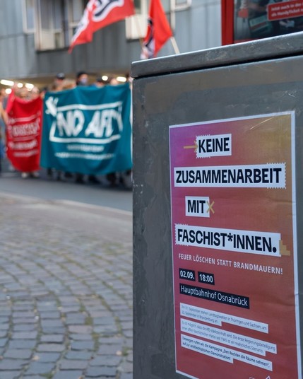 Im Vordergrund ein öffentlicher Mülleimer mit einem Plakat. 

Plakattext:
Keine Zusammenarbeit mit Faschist*innen 

Im Hintergrund unscharf Demomzug.