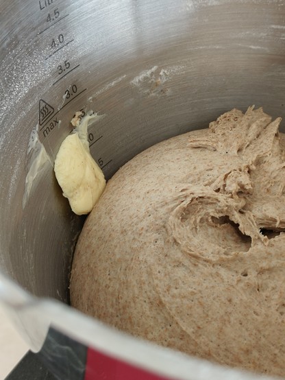 Butterstück klebt an der Wand der metallenen Rührschüssel über dem aufgehendem Teig. 