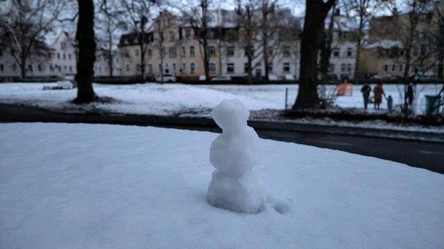 Das Bild zeigt einen kleinen Schneemann auf einem Autodach im Vordergrund. Im Hintergrund sind Gebäude, Bäume und einige Personen zu sehen, die sich auf einer schneebedeckten Fläche aufhalten. Dazwischen verläuft eine Straße mit getautem Schnee und Schneematsch.


Kopieren

