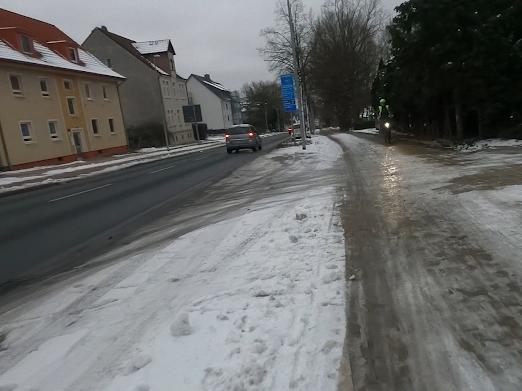 Auf einem vereisten Radweg kommt ein Radfahrer entgegen. Seine Beleuchtung spiegelt sich in der Eisfläche.